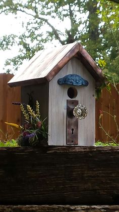 a bird house sitting on top of a wooden fence next to flowers and greenery