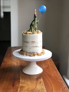 a birthday cake with a dinosaur on top and a blue balloon in the shape of a dog