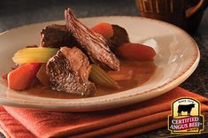 a white plate topped with beef and carrots next to a cup of coffee on top of a table