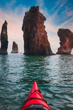 a red kayak is in the water near some rocks and an island with two large rock formations