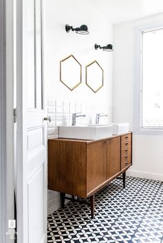 a bathroom with black and white tile flooring and wooden vanity, two mirrors above the sink