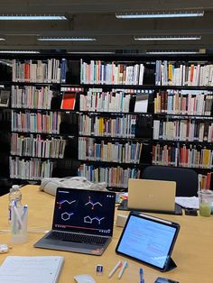 two laptops are sitting on a table in front of a bookshelf full of books