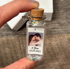 a hand holding a tiny glass bottle with a photo inside and a cork top lid