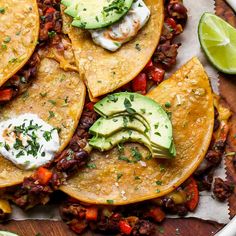 three tacos with beans, avocado and sour cream on top are sitting on a wooden platter