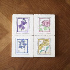 four stamps with flowers on them are sitting on a table top, one has purple and yellow flowers in the middle