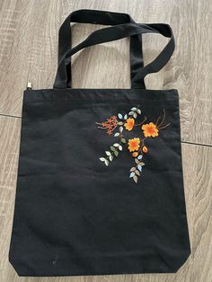 a black bag with orange flowers on it sitting on a wooden floor next to a pair of scissors