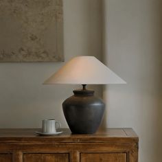 a table lamp sitting on top of a wooden cabinet next to a cup and saucer