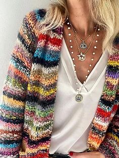 a woman with blonde hair wearing a multicolored cardigan sweater and jeans, holding a cell phone