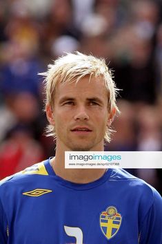 a man with blonde hair standing in front of a crowd wearing a blue shirt and holding a soccer ball