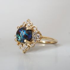 Immerse yourself in the mystique of the night with the Nocturne Ring, an enchanting piece featuring a mesmerizing black opal as its centerpiece. The opal’s swirling depths of dark blues and greens, capture the allure of a starlit sky. Set in an intricate gold floral frame adorned with brilliant diamonds. The ring evokes the quiet power of the night, making it a stunning statement piece for those who appreciate the blend of mystery and refined artistry. Handcrafted in your choice of 14K and 18K g Opal And Black Diamond Ring, Black Opal Gold Ring, Elegant Black Opal Ring As Gift, Elegant Black Opal Ring Gift, Luxury Black Opal Ring, Elegant Style, Starlit Sky, Black Opal Ring, Floral Frame, Gold Floral