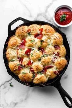 a cast iron skillet filled with bread and cheese covered in tomato sauce next to a bowl of ketchup