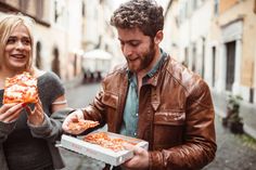 a man and woman are eating pizza on the street while standing next to each other