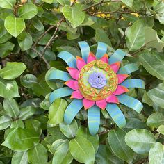 a paper sunflower sitting on top of a tree branch in the middle of leaves