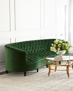 a green velvet couch in a living room next to a table with flowers on it