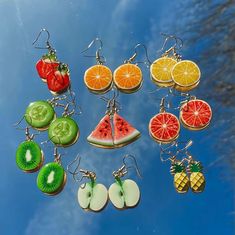 a collection of fruit shaped earrings hanging from hooks on a blue sky background with clouds