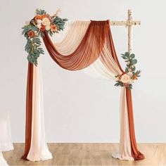 an orange and white wedding arch with flowers on the top is decorated with silk draping