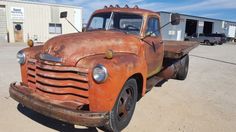 an old rusted out truck parked in a parking lot next to other trucks and buildings