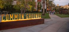 a sign that says common grounds in front of palm trees and people walking down the sidewalk