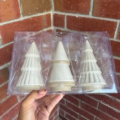 three small white cones are in a plastic package on a brick wall background, with one being held up to the camera