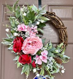 a wreath with pink and red flowers hanging from the front door, next to a beer can