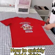 a person sitting at a table with a red t - shirt that says how to quickly fold it shirts