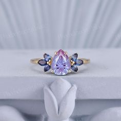 a close up of a ring with a pink and blue stone in the center on a white surface