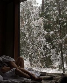 a woman laying on top of a bed in front of a window covered in snow