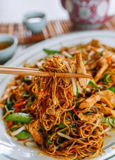 a white plate topped with noodles and meat next to chopsticks on a table