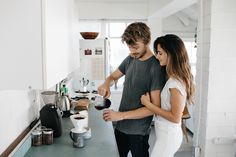 a man and woman standing in front of a kitchen counter pouring something into a cup