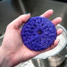 a hand holding a purple object in front of a metal bowl with water on it