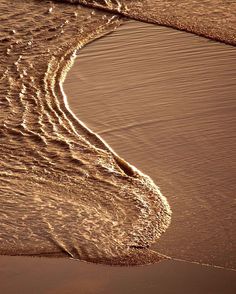 an ocean wave is coming in to the shore at sunset or sunrise, with light reflecting off the sand