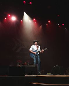 a man standing on top of a stage with a guitar in front of red and white lights