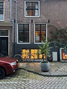 a red car parked in front of a tall brick building next to a bicycle rack