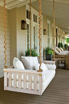 a porch swing with pillows on it and potted plants hanging from the front door