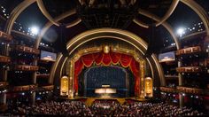 an auditorium full of people with red curtains on the stage and lights on the ceiling