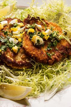 two crab cakes with lemon wedges and parsley sprouts on a plate