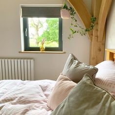 a bed with pink sheets and pillows in front of a window that has a green plant hanging over it