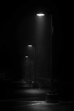 a black and white photo of two street lights in the dark with no one on it