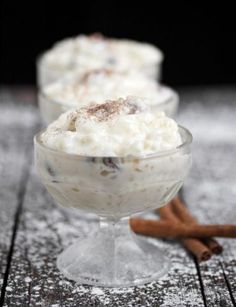 two desserts with cinnamon sticks and whipped cream in small glasses on a wooden table