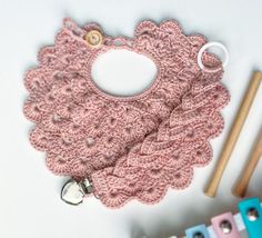 a pink crocheted bib next to some knitting needles