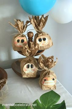 some paper bags with faces on them sitting on a table next to blue and white balloons