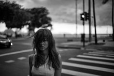 a woman standing on the side of a road next to a traffic light and palm trees