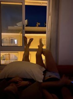 two people laying in bed with their feet up on the window sill and looking out