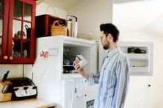 a man standing in front of an open refrigerator holding a carton of milk and looking at it