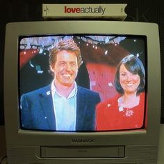 an old television set with a man and woman on it's screen, in front of a love actually sign