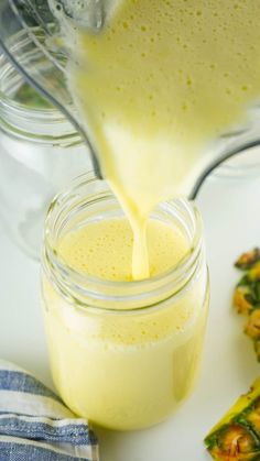 someone pouring orange juice into a mason jar filled with asparagus and other vegetables