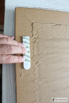 a person's hand on a piece of cardboard next to a box with tape