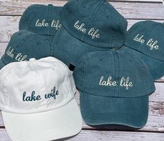 five lake life hats sitting on top of a wooden table next to a white baseball cap