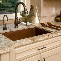 a kitchen with marble counter tops and brown sink faucet next to window overlooking trees