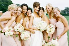 a group of women standing next to each other in front of a lush green field